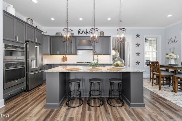 kitchen with decorative light fixtures, stainless steel appliances, and an island with sink