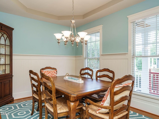 dining area with an inviting chandelier, a tray ceiling, and wood-type flooring