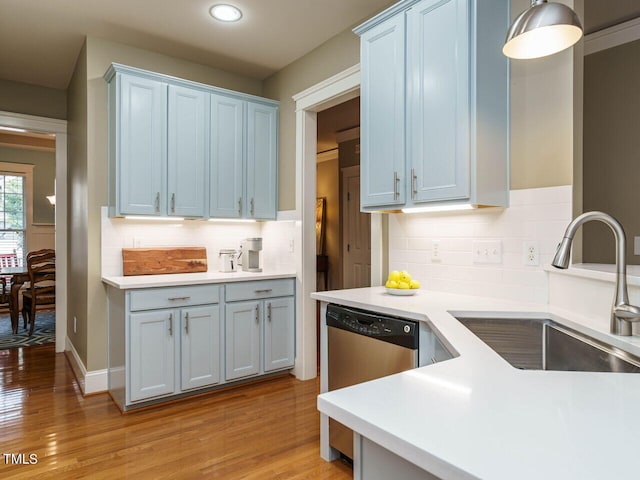 kitchen featuring pendant lighting, sink, backsplash, stainless steel dishwasher, and light hardwood / wood-style floors