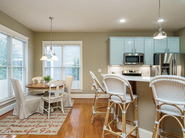 kitchen featuring appliances with stainless steel finishes, pendant lighting, white cabinets, backsplash, and light hardwood / wood-style floors