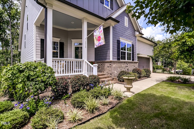 view of exterior entry featuring a garage, a lawn, and a porch