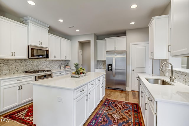 kitchen with sink, white cabinetry, a kitchen island, stainless steel appliances, and light hardwood / wood-style floors