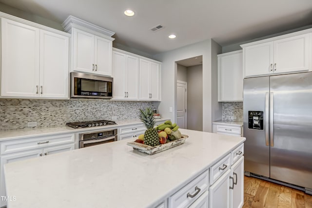 kitchen with tasteful backsplash, stainless steel appliances, white cabinets, and light wood-type flooring