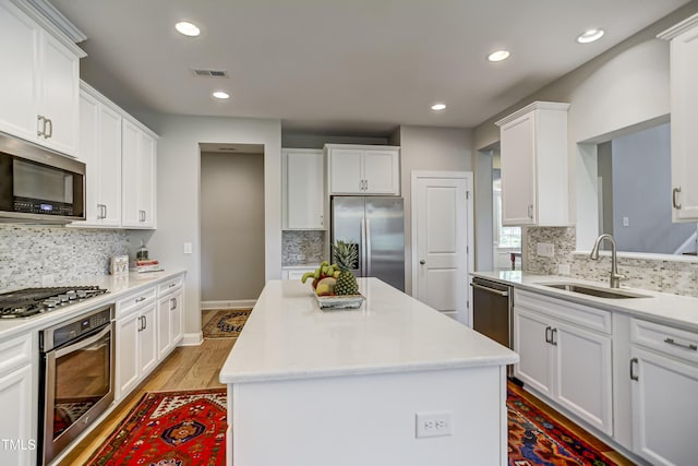 kitchen featuring stainless steel appliances, a center island, sink, and white cabinets