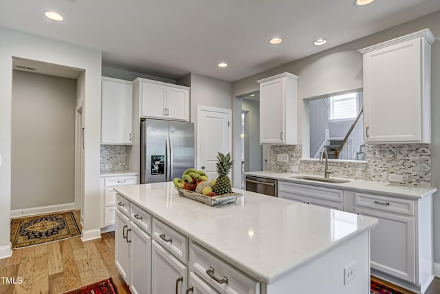 kitchen with sink, white cabinetry, light wood-type flooring, appliances with stainless steel finishes, and a kitchen island