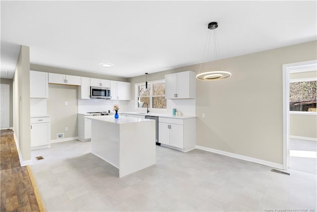 kitchen with decorative light fixtures, sink, white cabinets, a center island, and stainless steel appliances