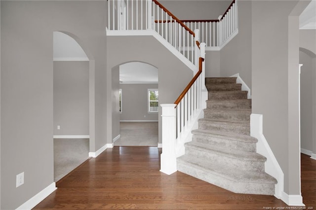 stairs with hardwood / wood-style flooring, ornamental molding, and a high ceiling