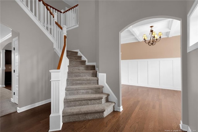 staircase with coffered ceiling, hardwood / wood-style floors, a notable chandelier, and beam ceiling