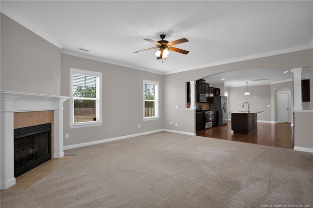 unfurnished living room featuring sink, ceiling fan, ornamental molding, a tiled fireplace, and dark carpet