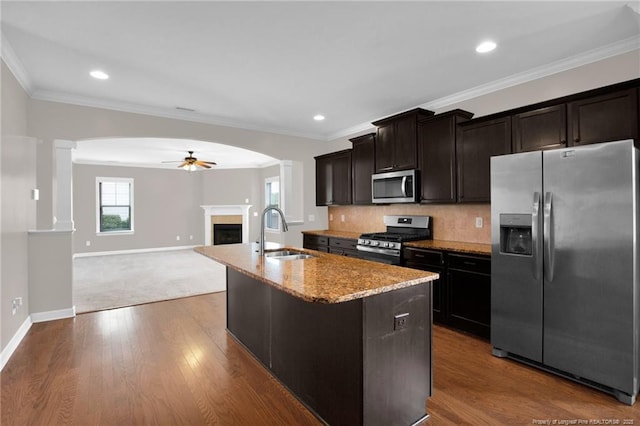 kitchen featuring sink, ceiling fan, stainless steel appliances, light stone countertops, and an island with sink