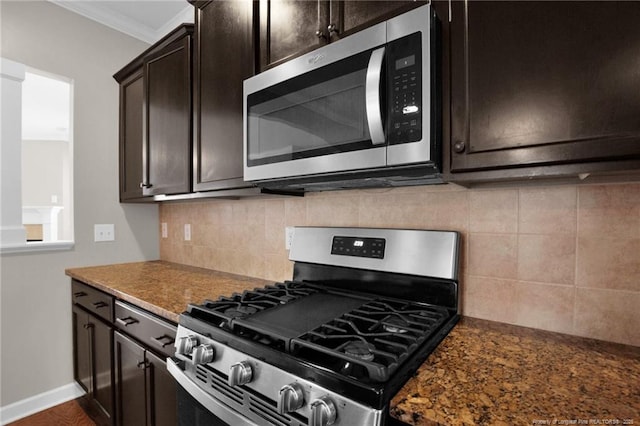 kitchen featuring dark brown cabinets, dark stone countertops, ornamental molding, appliances with stainless steel finishes, and backsplash