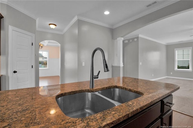 kitchen with sink, light carpet, dark stone countertops, ornamental molding, and decorative columns