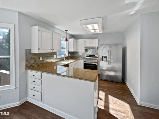 kitchen with appliances with stainless steel finishes, white cabinetry, sink, dark stone counters, and kitchen peninsula