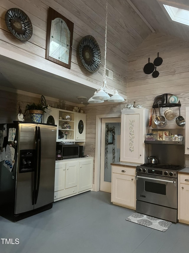 kitchen with hanging light fixtures, wooden walls, stainless steel appliances, a skylight, and white cabinets