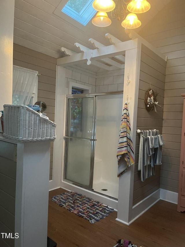 bathroom featuring hardwood / wood-style flooring, wooden walls, a skylight, and a shower with shower door