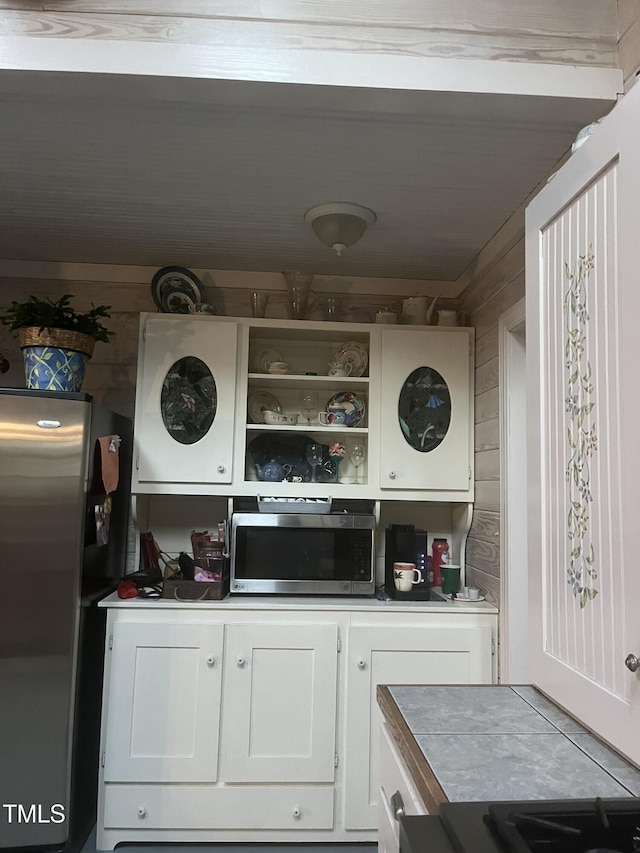 kitchen featuring appliances with stainless steel finishes, white cabinets, and wood walls