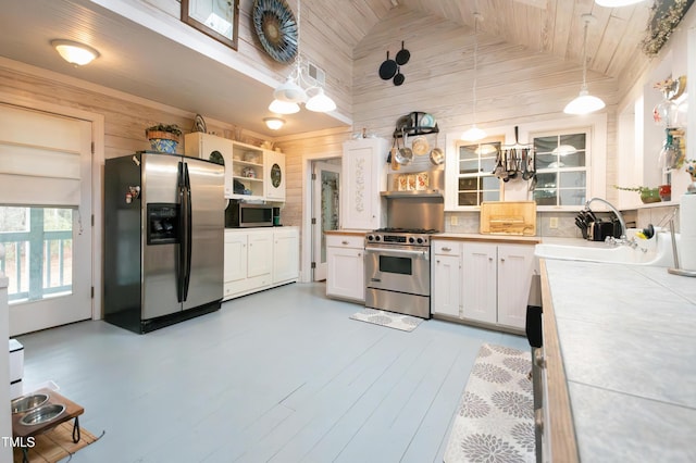 kitchen featuring sink, white cabinetry, decorative light fixtures, appliances with stainless steel finishes, and wooden walls