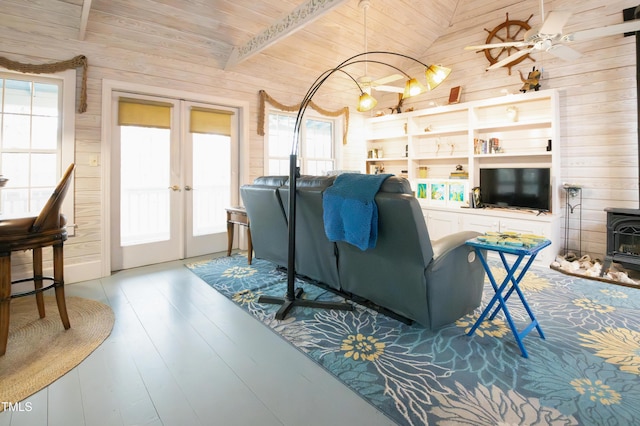 living room with french doors, wooden walls, vaulted ceiling, and a wood stove