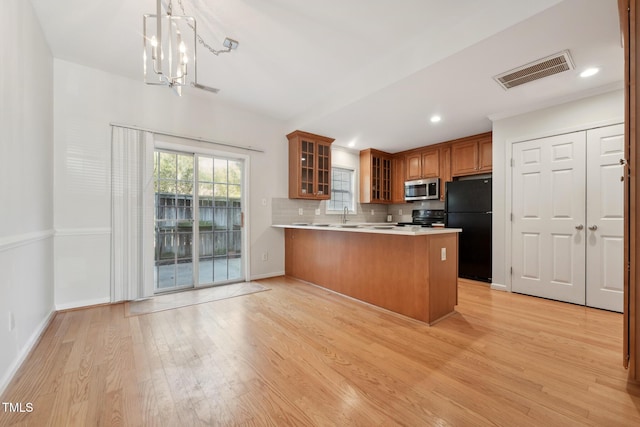 kitchen with decorative light fixtures, black appliances, backsplash, light hardwood / wood-style floors, and kitchen peninsula