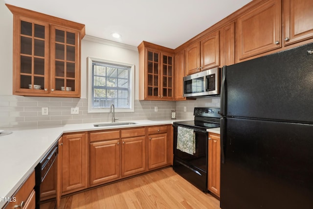 kitchen featuring sink, tasteful backsplash, ornamental molding, light hardwood / wood-style floors, and black appliances