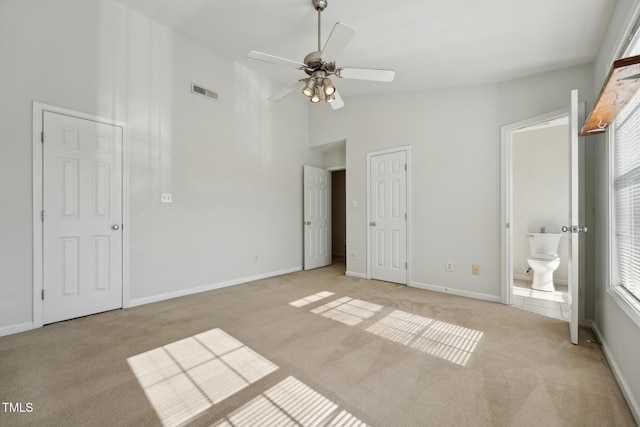 unfurnished bedroom featuring high vaulted ceiling, light colored carpet, ceiling fan, and ensuite bathroom