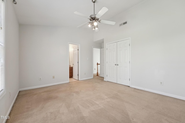 unfurnished bedroom with ensuite bath, ceiling fan, high vaulted ceiling, light carpet, and a closet