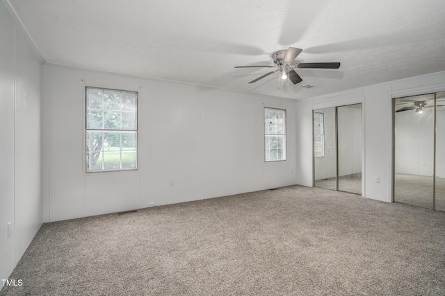 unfurnished bedroom featuring multiple closets, ceiling fan, carpet floors, and a textured ceiling