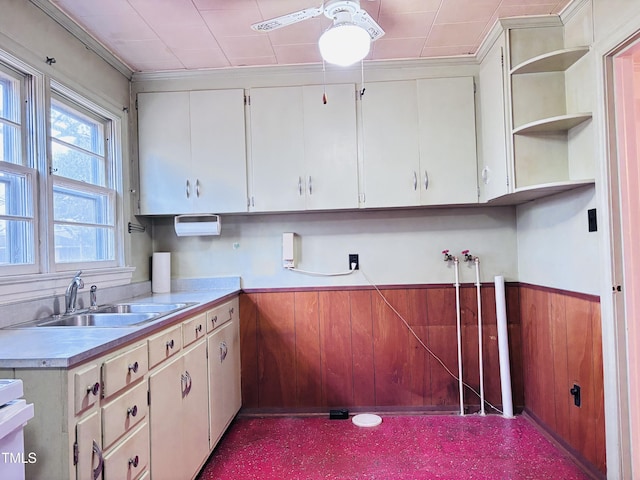 kitchen with ceiling fan, wooden walls, sink, and white cabinets