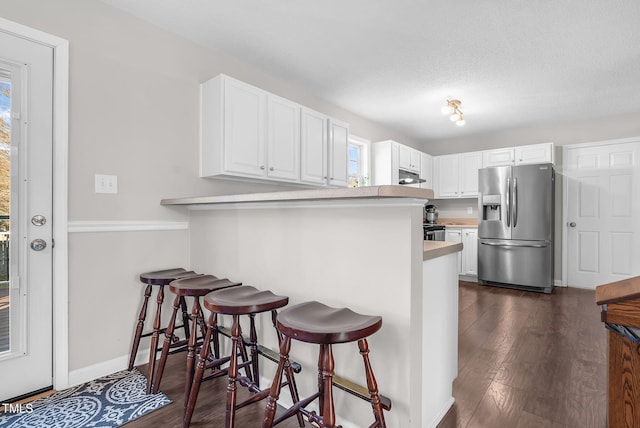 kitchen featuring dark hardwood / wood-style floors, stainless steel refrigerator with ice dispenser, white cabinets, a kitchen bar, and kitchen peninsula