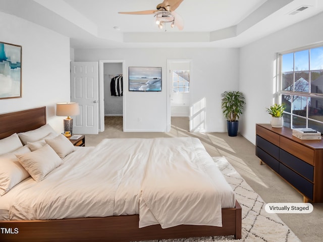 carpeted bedroom featuring ceiling fan, ensuite bath, a tray ceiling, and a spacious closet