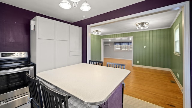 kitchen featuring white cabinetry, a kitchen breakfast bar, a notable chandelier, light wood-type flooring, and stainless steel electric range