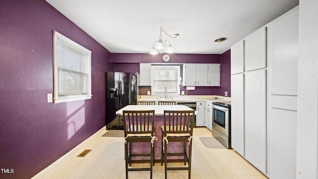 kitchen featuring stainless steel range with electric cooktop, a chandelier, black refrigerator with ice dispenser, hanging light fixtures, and white cabinets