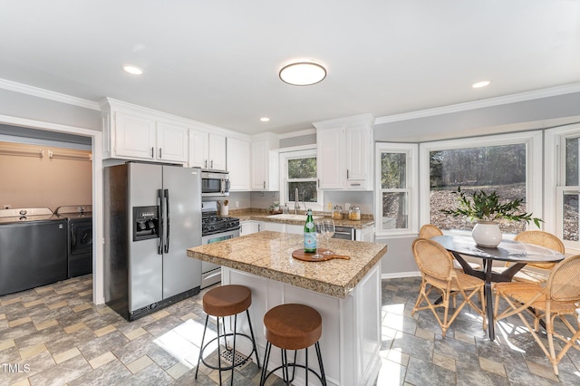 kitchen featuring crown molding, a center island, appliances with stainless steel finishes, washer and clothes dryer, and white cabinets