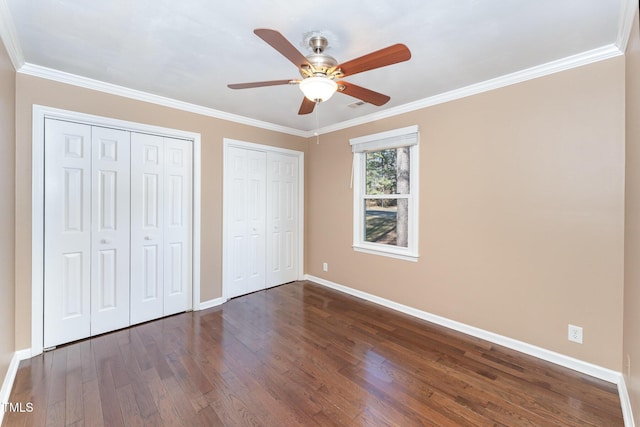 unfurnished bedroom with multiple closets, dark hardwood / wood-style floors, and crown molding