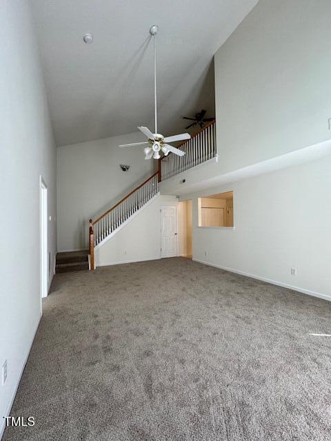 unfurnished living room featuring a towering ceiling, ceiling fan, and carpet