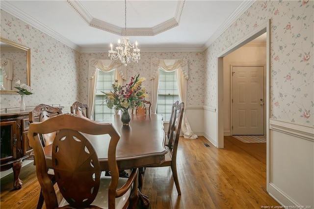 dining space featuring a chandelier, ornamental molding, a raised ceiling, and hardwood / wood-style floors