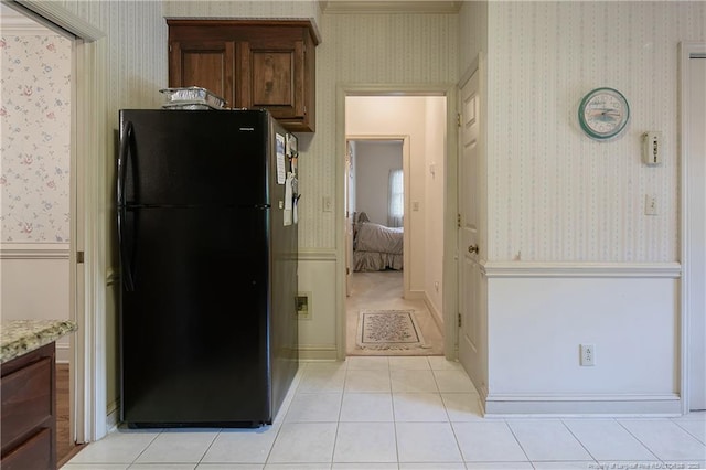 kitchen with light tile patterned flooring, black refrigerator, and light stone counters