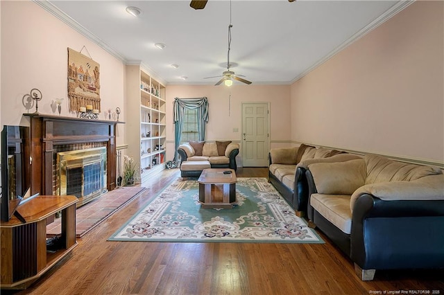 living room featuring built in shelves, ornamental molding, hardwood / wood-style flooring, ceiling fan, and a fireplace