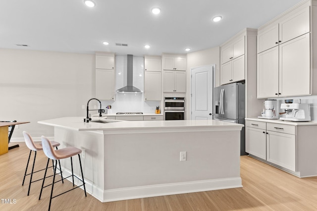 kitchen with white cabinetry, an island with sink, and wall chimney range hood