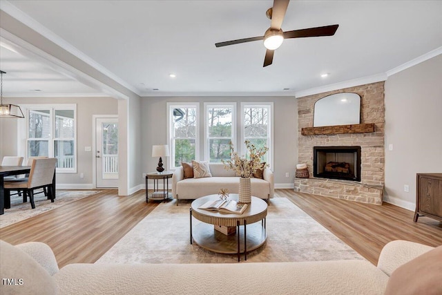 living room featuring crown molding, a stone fireplace, light hardwood / wood-style floors, and ceiling fan