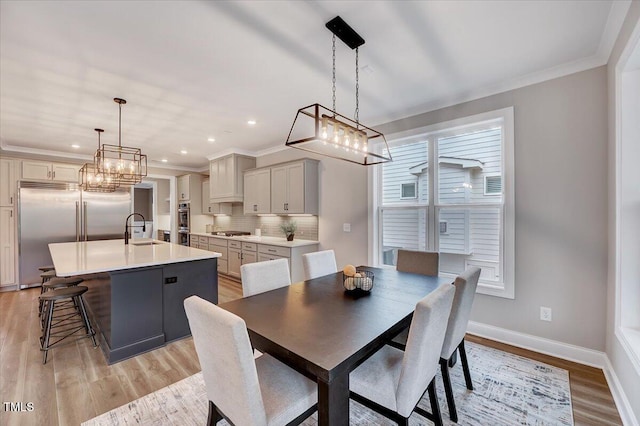 dining room with sink, crown molding, and light hardwood / wood-style flooring