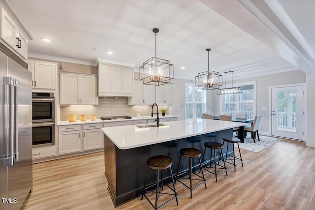 kitchen with sink, a breakfast bar, stainless steel appliances, an island with sink, and decorative light fixtures