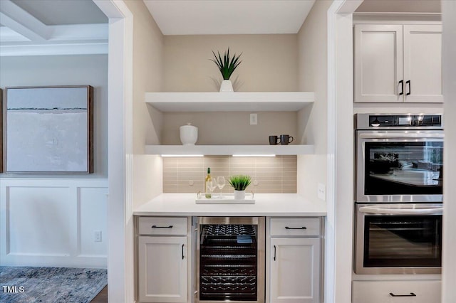 bar featuring white cabinetry, stainless steel double oven, beverage cooler, and tasteful backsplash