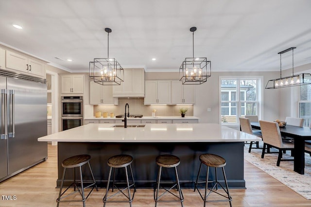 kitchen featuring white cabinetry, hanging light fixtures, stainless steel appliances, and a center island with sink