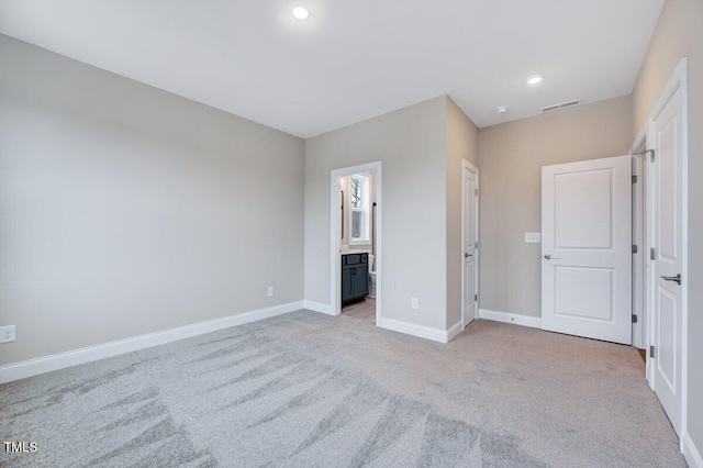 unfurnished bedroom featuring light carpet and ensuite bath