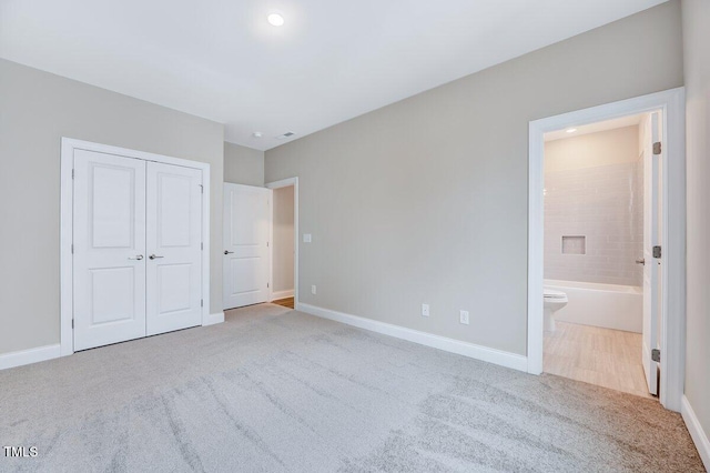 unfurnished bedroom featuring light colored carpet, ensuite bath, and a closet