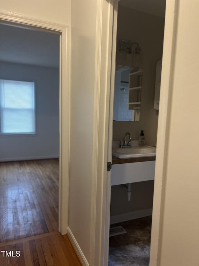 hall featuring visible vents, baseboards, a sink, and wood finished floors