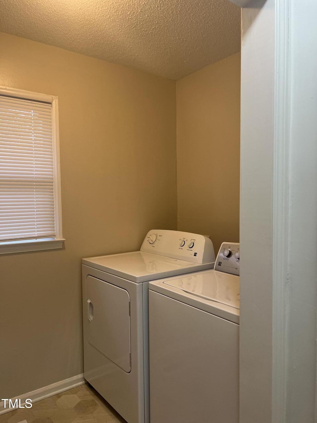 clothes washing area featuring a textured ceiling, laundry area, washing machine and dryer, and baseboards