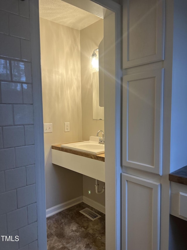 bathroom featuring a textured ceiling, a sink, visible vents, and baseboards