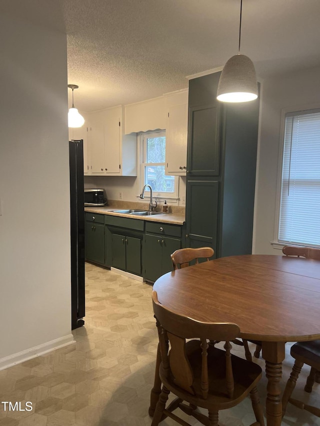 kitchen featuring green cabinets, light countertops, a textured ceiling, pendant lighting, and a sink